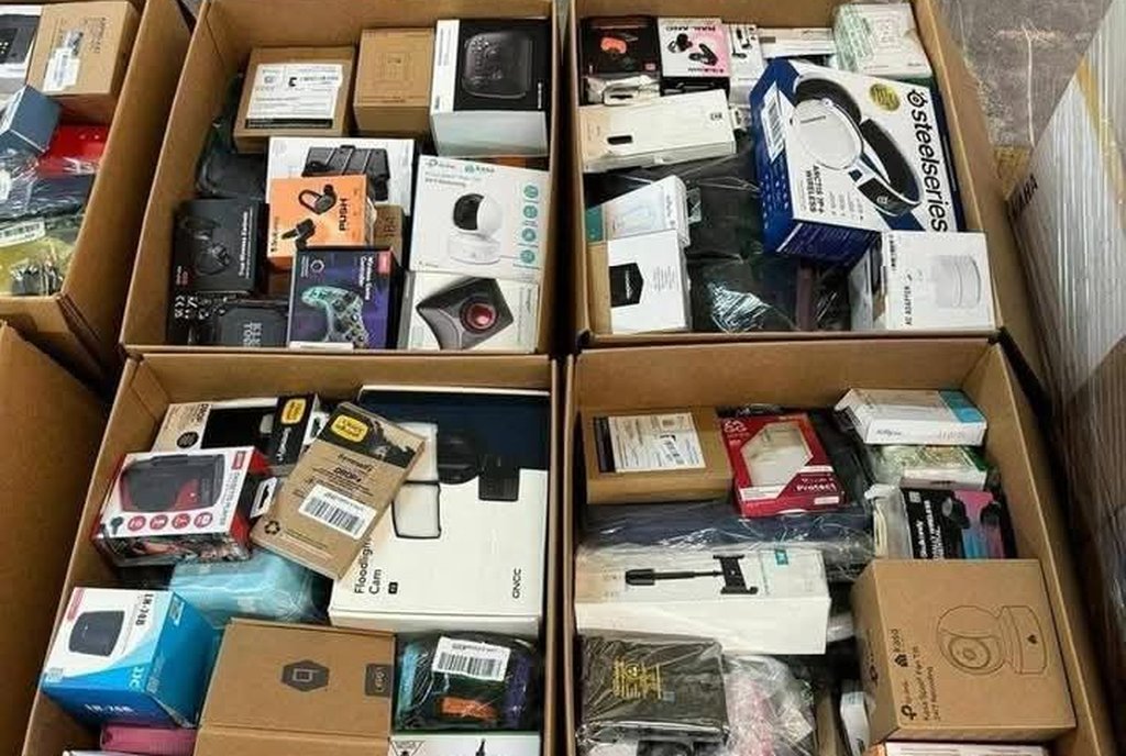 Quatro caixas de um palete aberto cheias de eletrônicos lacrados: fones, câmeras, controles e acessórios