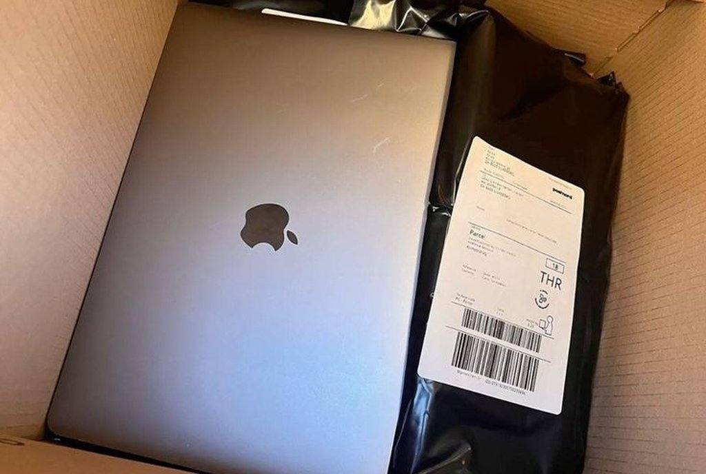 Caixa de papelão aberta com um MacBook Pro e um pacote lacrado com etiqueta de envio dentro